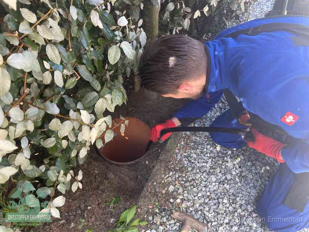 Een monteur voert een slang in een geopende rioolput in de tuin om het hoofdriool te ontstoppen in Emmeloord